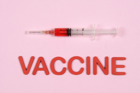 vaccine word written in red with syringe on light pink background