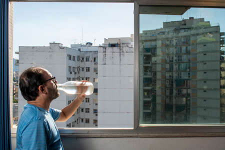 man drinking water from the bottle at the window during pandemicの写真素材