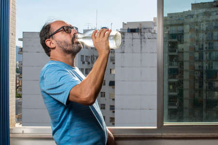 man drinking water from the bottle at the window during pandemicの写真素材
