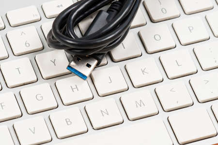 USb cable wrapped around white computer keyboard.の写真素材