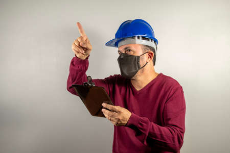 civil industry worker man with blue helmet and clipboard in hand pointing upwardsの写真素材