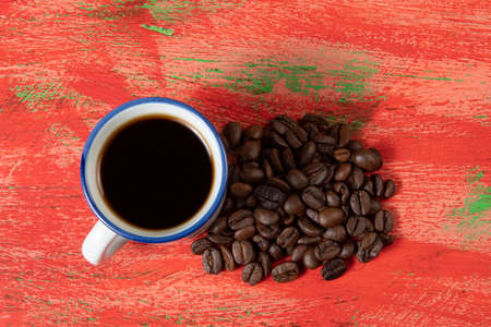 small coffee cup with beans on the side and rustic red tableの写真素材