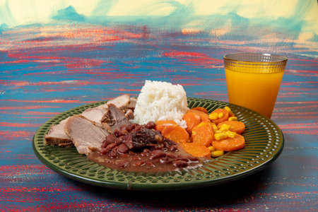 Typical Brazilian food dish with rice, red beans, pork and carrot salad and braised corn in a green plateの写真素材