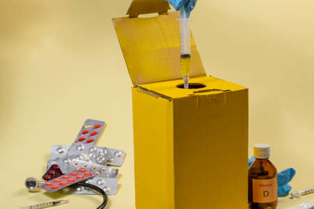 yellow disposal box for contaminated or infectious products in a hospital or home. hand putting the syringeの写真素材