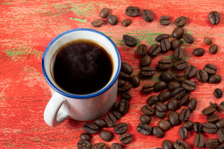 small coffee cup with beans on the side and rustic red tableの写真素材
