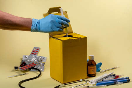 yellow disposal box for contaminated or infectious products in a hospital or home. hand putting the syringeの写真素材