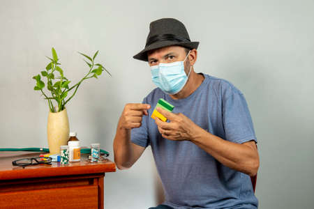 59-year-old man taking medicine to take care of his physical health, using mask and hatの写真素材