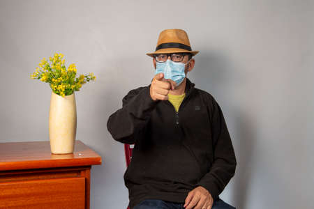 man sitting on a chair and pointing with his finger, wearing a hat.の写真素材