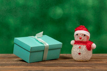 Green gift box with polka dots on rustic wooden background and a snow dollの写真素材