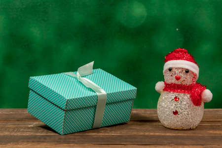Green gift box with polka dots on rustic wooden background and a snow dollの写真素材