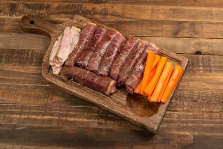 beef roll raw to prepare with bacon and carrots on a kitchen boardの写真素材