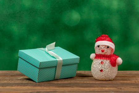 Green gift box with polka dots on rustic wooden background and a snow dollの写真素材