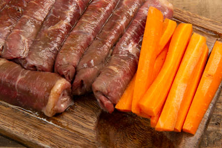 beef roll raw to prepare with bacon and carrots on a kitchen boardの写真素材