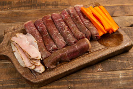 beef roll raw to prepare with bacon and carrots on a kitchen boardの写真素材