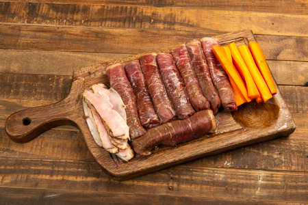 beef roll raw to prepare with bacon and carrots on a kitchen boardの写真素材