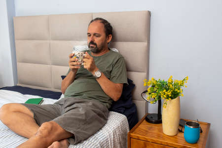 Senior man sitting on bed drinking coffeeの写真素材