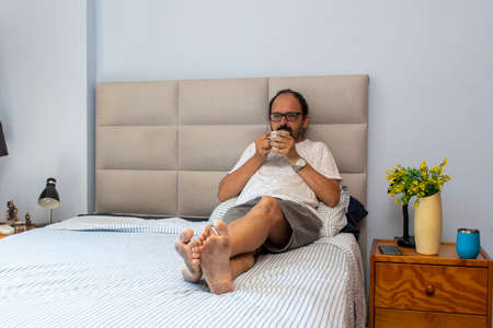 Senior man sitting on bed drinking coffeeの写真素材