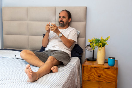 Senior man sitting on bed drinking coffeeの写真素材