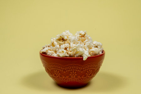 A ceramic bowl of salted popcorn on the yellow table.の写真素材