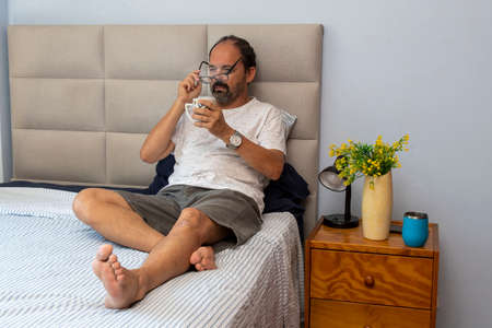 Senior man sitting on bed drinking coffeeの写真素材