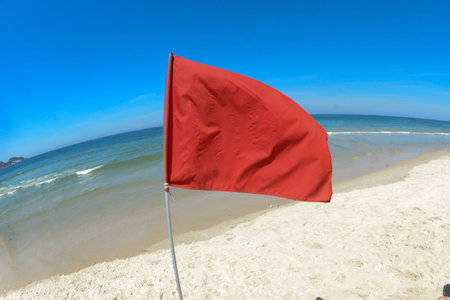 red flag on the beach indicating danger zone for swimming, in a blue sky
