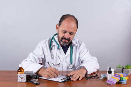 Portrait of senior mature doctor writing on prescription looking downの写真素材