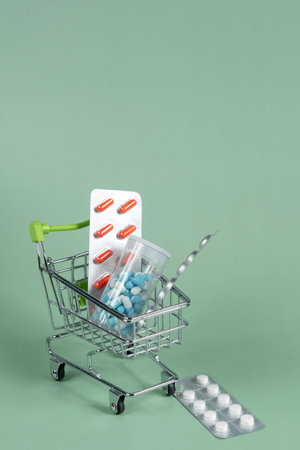 several different packages of pills in small shopping car on green background, medicine order...