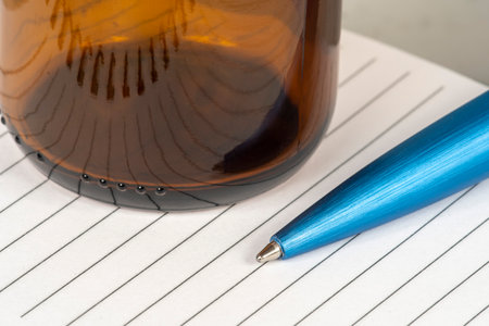 ballpoint pen on lined paper pad with empty amber glassの写真素材