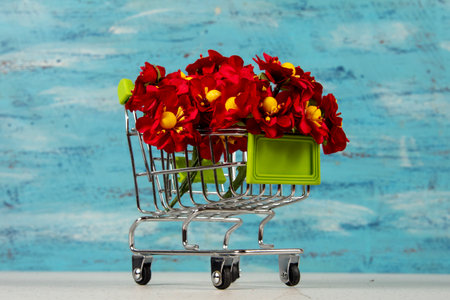 shopping cart with red artificial flowers on blue backgroundの写真素材