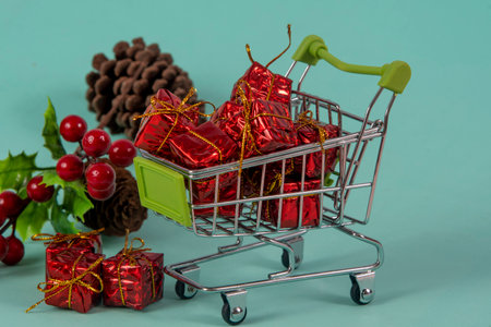 Christmas shopping cart with gifts and Christmas tree in background on light green background, selective focusの写真素材