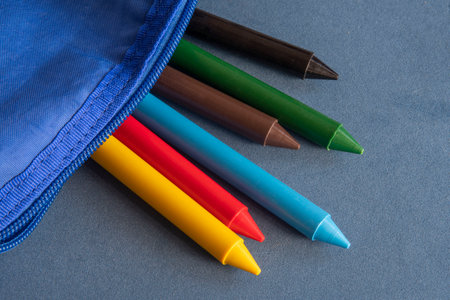 crayon pencil sticking out of a school case representing back to school over blue tableの写真素材