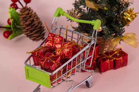 Christmas shopping cart with gifts and Christmas tree in background on light red backgroundの写真素材