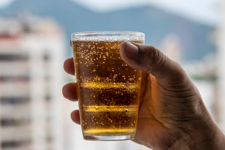 man holding glass of beer on blurred urban city background with building and mountainsの写真素材
