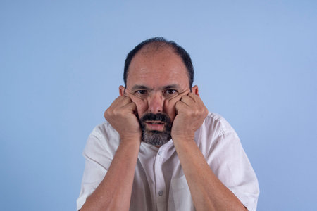 Portrait of 60 years old bearded man on blue background expression face