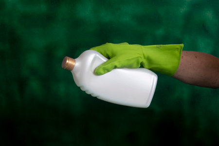 Hand with protective glove holding packaging of cleaning products used for home hygiene in a green backgroundの写真素材