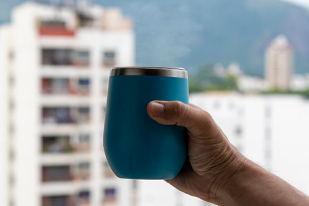 hand holding a mug of water with a view on the city background on fesfocusの写真素材