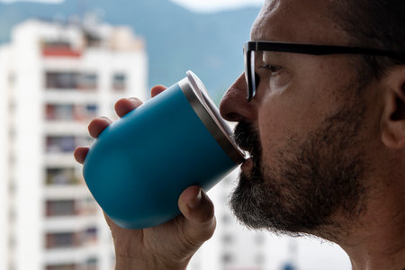 man drinking water from blue mug with view on blurred city backgroundの写真素材