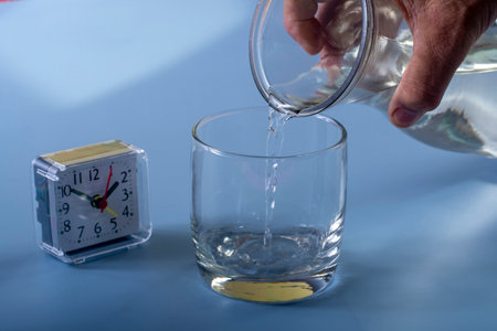 Detail of the person filling the glass with water. Concept of reminding hydration time on blue backgroundの写真素材