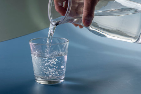 Detail of person filling glass of water. hydration concept in blue backgroundの写真素材