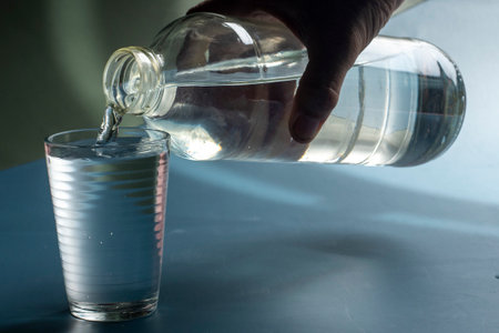 Detail of person filling glass of water. hydration concept in blue backgroundの写真素材