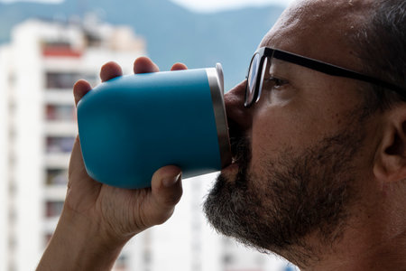 man drinking water from blue mug with view on blurred city backgroundの写真素材
