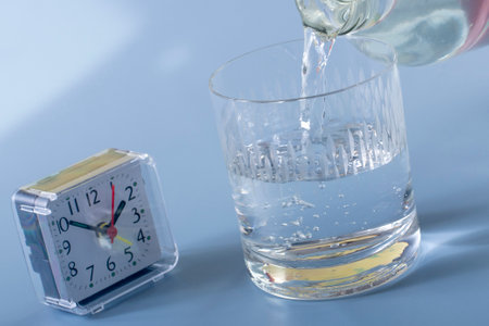 Detail of the person filling the glass with water. Concept of reminding hydration time on blue backgroundの写真素材