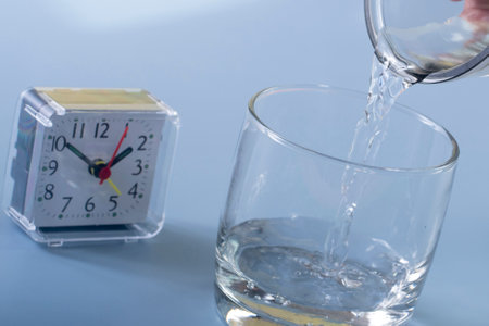 Alarm clock and a glass of water on a blue background.の写真素材