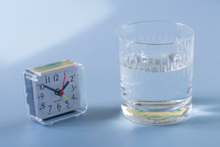 Alarm clock and a glass of water on a blue background.の写真素材