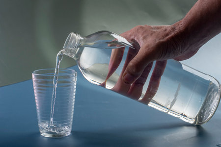 hand pouring water from a bottle into a glass on a blue backgroundの写真素材