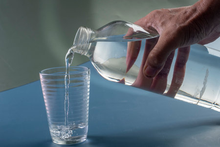 Detail of person filling glass of water. hydration concept in blue backgroundの写真素材