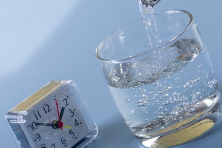 Detail of the person filling the glass with water. Concept of reminding hydration time on blue backgroundの写真素材