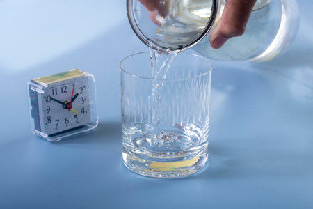 Detail of the person filling the glass with water. Concept of reminding hydration time on blue backgroundの写真素材