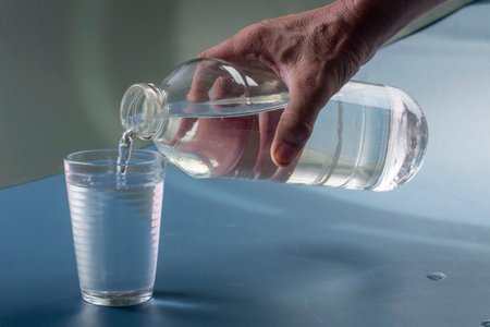 Detail of person filling glass of water. hydration concept in blue backgroundの写真素材