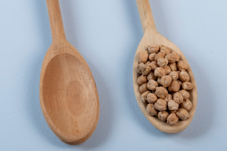 wooden spoon with chickpeas with another empty one in blue backgroundの写真素材